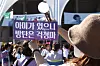 A fan holds up a purple BTS support sign while taking a photo at Busan Asiad Main Stadium.