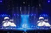 Blue concert stage with large screens showing a performer and crowd silhouettes below.