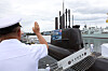 Royal Canadian Navy officer saluting a Korean submarine and frigate at a harbor ceremony.
