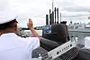 Royal Canadian Navy officer saluting a Korean submarine and frigate at a harbor ceremony.