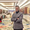 Casimir Agossou stands smiling with arms crossed in a hotel hallway.