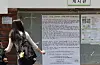 Student stands by a campus bulletin board with a large protest notice about ballot paper shortages.