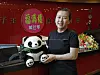 A woman stands next to a large panda mascot figure at a restaurant counter with a red sign behind her.