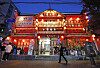 Red-lit restaurant storefront with pedestrians walking past on a street at dusk.