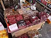 Outdoor market stall displaying assorted packaged snacks and dried goods in trays and bags.