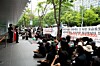 Crowd of protesters seated and standing on a sidewalk beside a building, holding banners with Korean text.