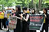 People standing outdoors holding protest signs and a banner near trees on a city street.