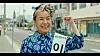 A smiling candidate wears a sign and raises a fist on a town street.