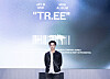 A man stands on stage before a large promotional screen for the mini album 'TR.EE.'