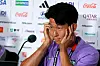 Son Heung-min at a press conference, holding his face with microphones and sponsor logos in the background.