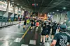 A group of runners moves through a spacious indoor hall with marked lanes and people gathered along the sides.