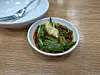 Bowl of asparagus topped with garlic on a wooden table next to plates and forks.