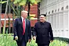 Donald Trump and Kim Jong-un walk side by side along a garden path near a hotel building.