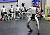 Unitree G1 humanoid robot dancing in front of seated robots at a trade show booth.
