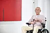 Park Seo-bo sits in a wheelchair beside a large red abstract painting in a white gallery.