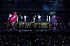 Performers on a lit stage in front of a large audience in a dark arena.