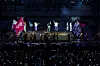 Performers on a lit stage in front of a large audience in a dark arena.