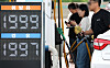 People refuel cars at a Seoul gas station beside digital fuel price signs.
