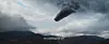 Dark glowing object in a cloudy sky over mountains.