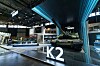 Trade show booth with a large illuminated K2 sign and digital displays in a convention center.