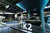 Trade show booth with a large illuminated K2 sign and digital displays in a convention center.