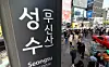 Crowds and vehicles move past a Seongsu (Musinsa) Station sign in Seoul.