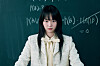 Young woman standing in front of a chalkboard with handwritten equations.