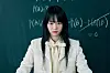Young woman standing in front of a chalkboard with handwritten equations.
