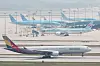 Passenger airplanes lined up on a runway at Incheon International Airport with a taxiing aircraft in the foreground.