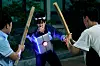 A man in protective gear faces two others holding wooden sticks during a nighttime training exercise.