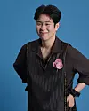 Man standing in front of a blue background wearing a dark shirt with a pink flower accent.