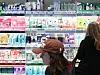 Two shoppers look at rows of Korean cosmetics displayed on lit shelves inside an Olive Young store.