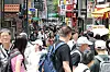 Crowds of people walk through a busy shopping street lined with signs and storefronts in Seoul.