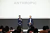 Two men seated on stage in front of an Anthropic logo, speaking to an audience.