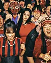 A dense group of people in colorful masks and face paint standing together indoors.