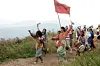 A group of people in traditional dress walking on a mountain trail with flags and drums.