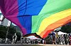 A large rainbow flag stretches overhead as parade participants march below in Seoul.