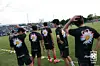 Soccer players in black shirts stand on the sideline near a grassy field.