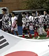 Soccer players in patterned warm-up tops walk beside a large flag near the sideline.