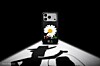 A floral smartphone case upright on a spotlighted surface, with a large shadow in front of it.