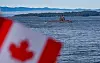 A Korean submarine sails on calm water near Esquimalt with a blurred Canadian flag in the foreground.