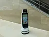 Small white service robot with a screen standing on a mall floor.