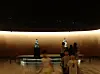 Visitors walk through a museum gallery with two statues on pedestals and a glowing curved wall.