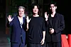 Three men pose onstage at a Netflix series press conference in Seoul, each raising a hand.