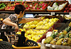 A shopper reaches toward a display of imported mangoes in a Seoul supermarket produce section.