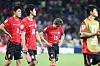 South Korea players in red jerseys stand disappointed on the field after a loss.
