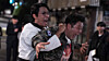 Taekwondo instructor holding back a man during a nighttime confrontation on a city street.