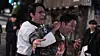 Taekwondo instructor holding back a man during a nighttime confrontation on a city street.