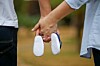A couple is holding hands while holding a pair of baby shoes