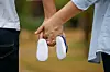 A couple is holding hands while holding a pair of baby shoes